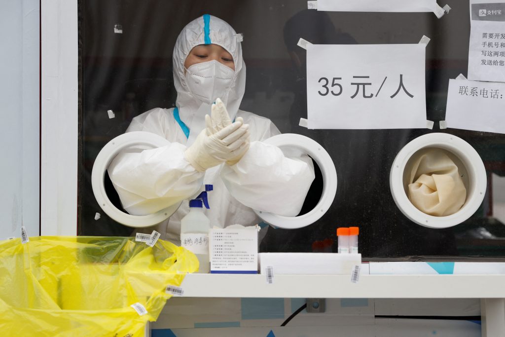 A medical worker wearing personal protective equipment (PPE) disinfects her gloves after conducting a test for the coronavirus…