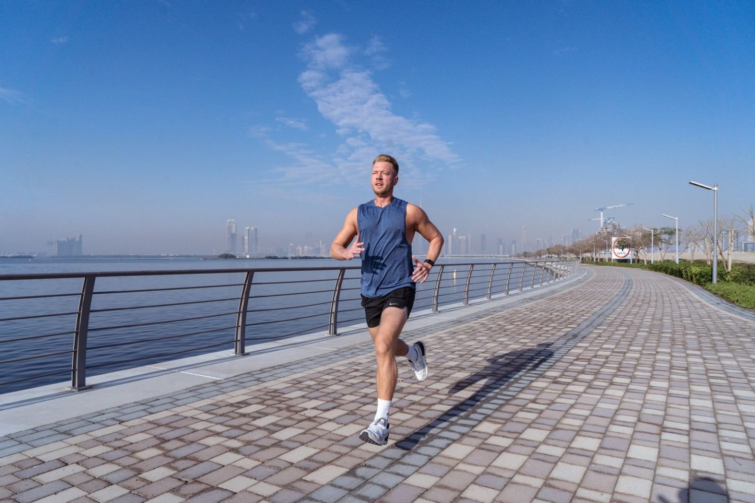 A runner jogging along a waterfront promenade on a sunny day